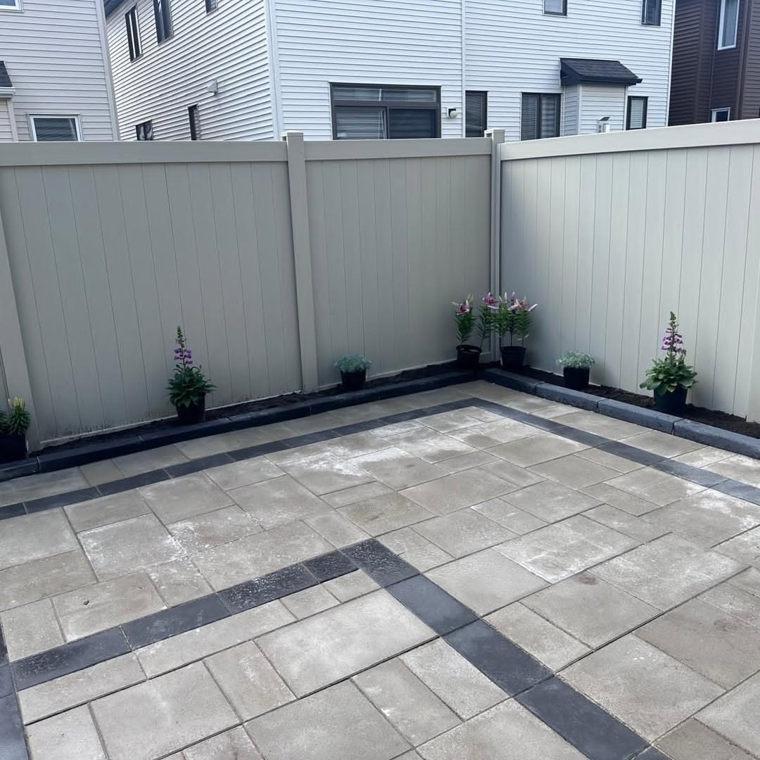 Backyard interlock paver patio with charcoal banding and vinyl privacy fence