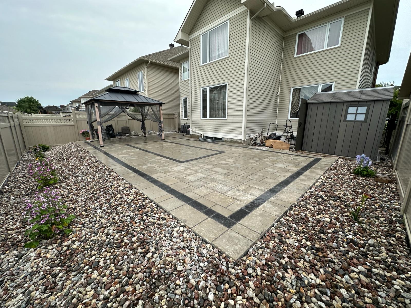Backyard interlock paver patio with charcoal banding, gazebo and pebble surround